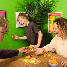 Load image into Gallery viewer, Family playing Stomp Stomp Chomp card game together with a green wall and plant in the background