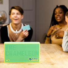 Load image into Gallery viewer, Board game box &quot;The Chameleon&quot; with people laughing and playing in the background
