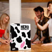 Load image into Gallery viewer, Board game box titled &#39;HERD MENTALITY&#39; with people playing in the background
