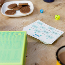 Load image into Gallery viewer, The Chameleon board game components on a wooden table with cookies and dice.
