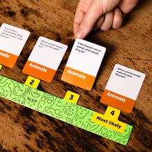 Load image into Gallery viewer, Dumb Questions To Ask Your Friends game with cards and a scoring track on a wooden surface
