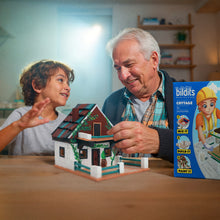 Load image into Gallery viewer, Man and child playing with a miniature house model, with a Biltits toy packaging in the background.
