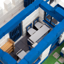 Load image into Gallery viewer, Toy model of a building with blue and white structure, including desks and chairs.
