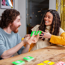 Load image into Gallery viewer, Two people playing the board game You Can&#39;t Say Umm together at a table with festive decorations in the background.
