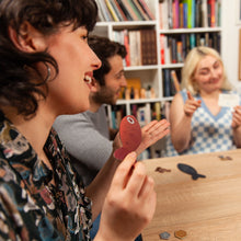 Load image into Gallery viewer, People playing the Sounds Fishy board game together in a cozy room with bookshelves.
