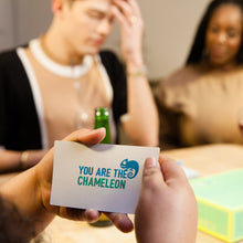 Load image into Gallery viewer, Person holding a card with &#39;You are the Chameleon&#39; text in a social setting.
